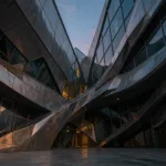 Deconstructivist museum with shattered colliding titanium and glass planes at dusk