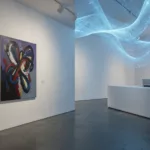Modern gallery interior split between a human abstract painting and glowing blue AI data flows